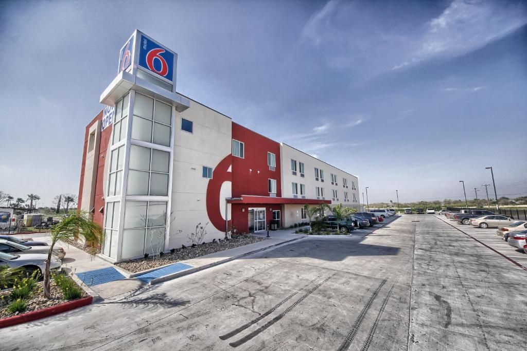 Un hotel con un llamativo logotipo con el número '6', un estacionamiento y un cielo despejado.