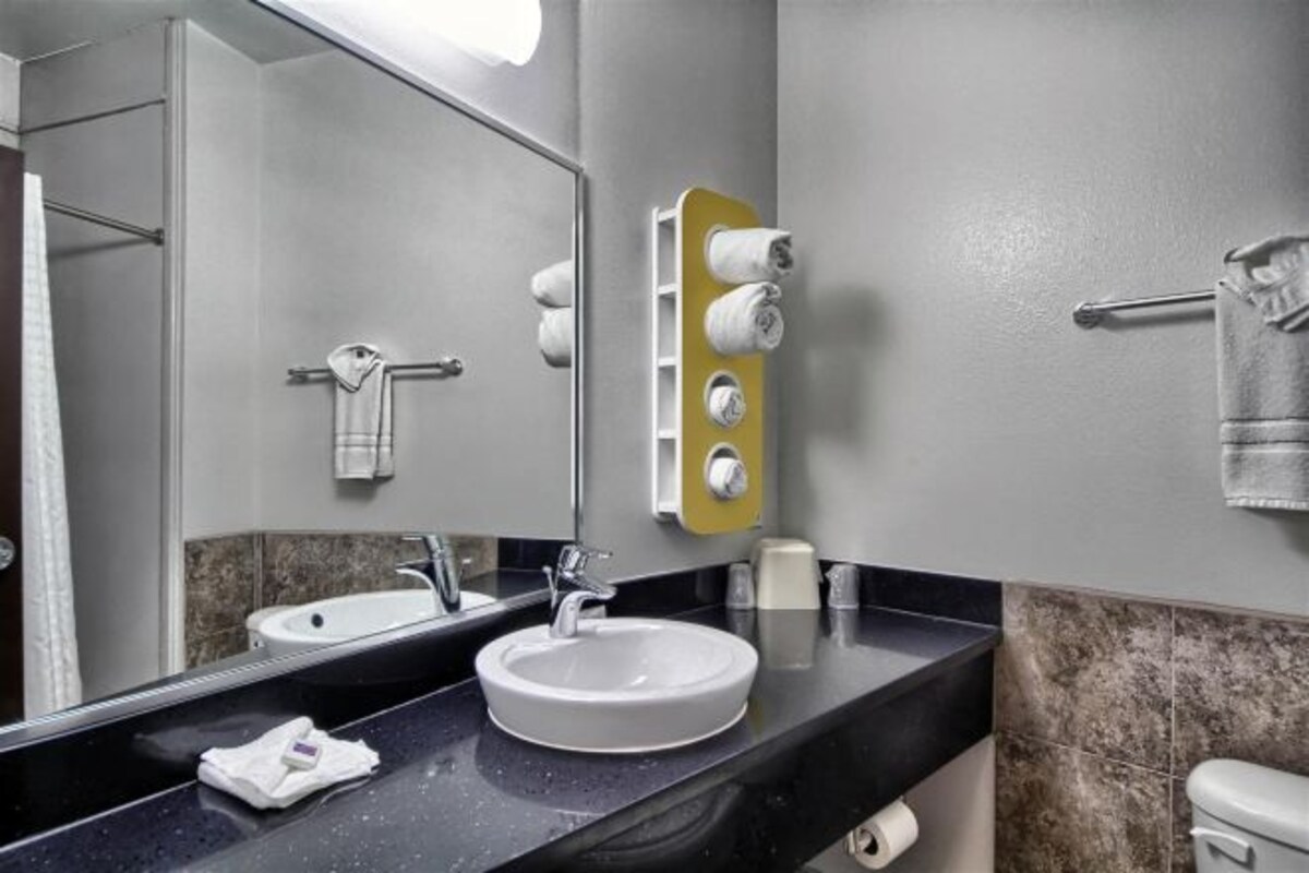 Un baño con lavamanos, espejo, toallero y retrete.