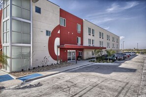 A modern building with a red and beige facade, large windows, and a parking lot with several cars. - Motel 6 Weslaco, TX (Weslaco)