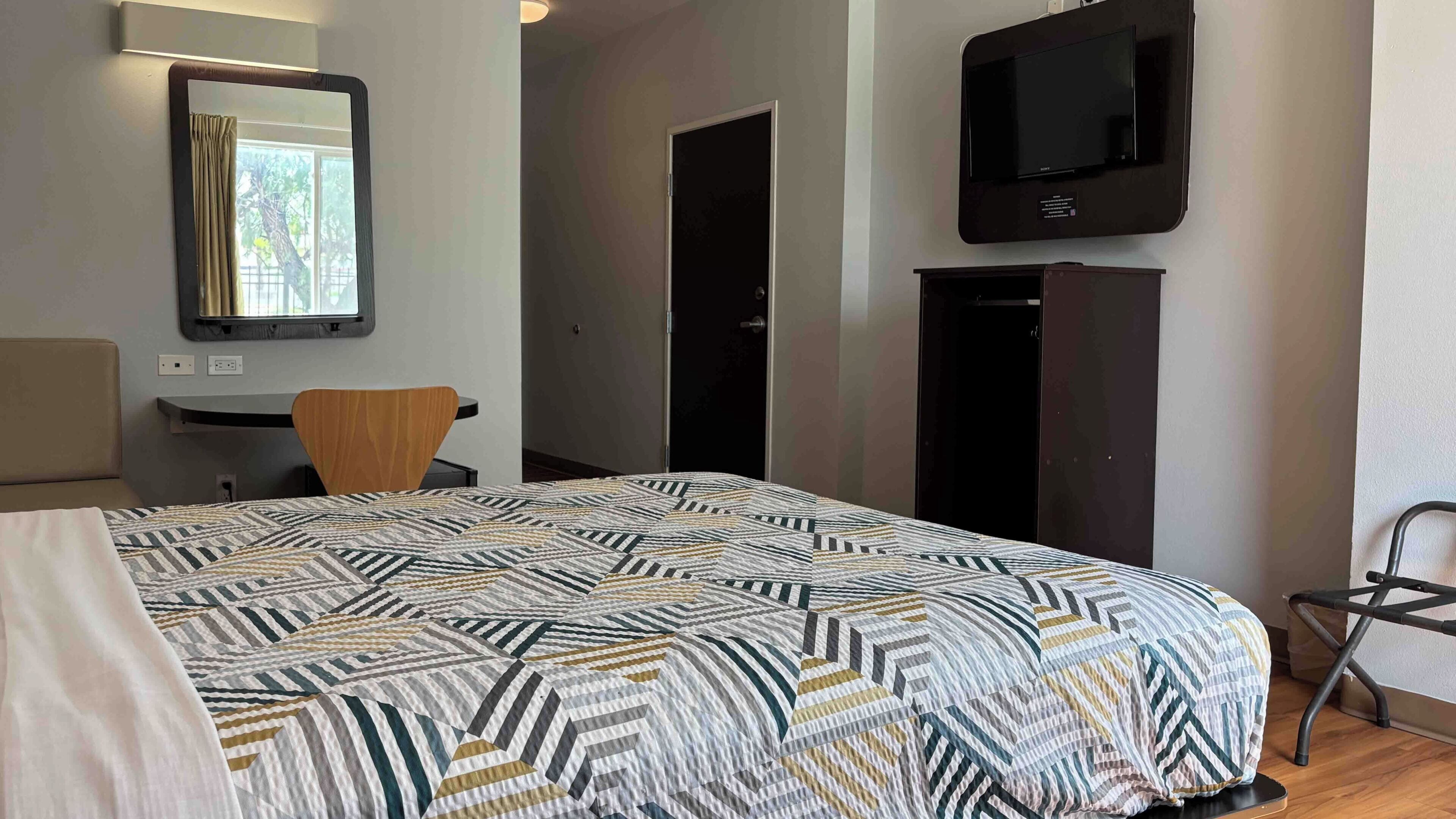 Habitación de hotel con cama, escritorio, silla, televisor y armario.