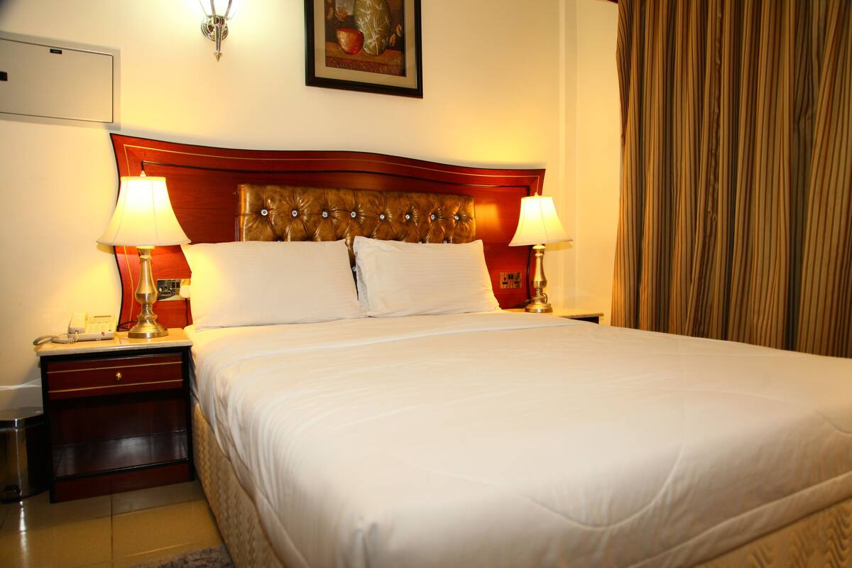 A hotel room with a large bed, two bedside lamps, a nightstand with a phone, and a painting on the wall.