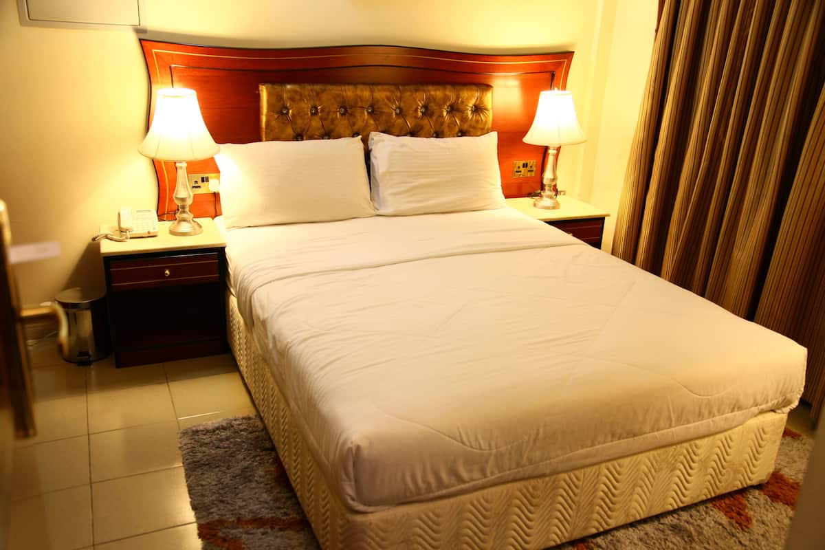A hotel room with a large bed, two bedside tables with lamps, a wooden headboard, and a patterned rug.