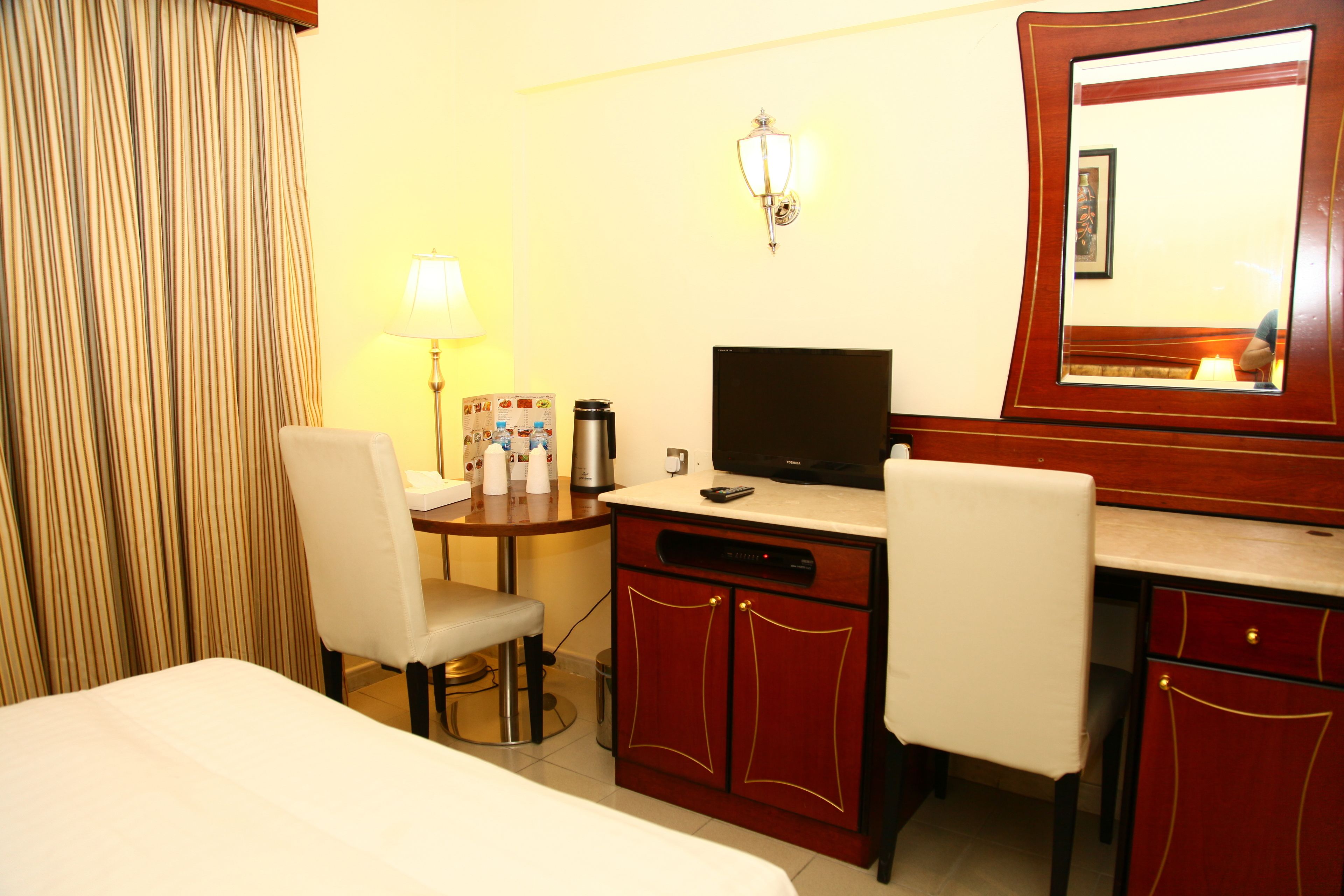 A hotel room with a bed, a desk with a television, a chair, a lamp, and a cabinet.