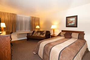 Une chambre d’hôtel avec un grand lit, deux tables de chevet avec des lampes, une chaise agrémentée d’un coussin à motifs équestres, un tableau au mur et une fenêtre avec des rideaux.