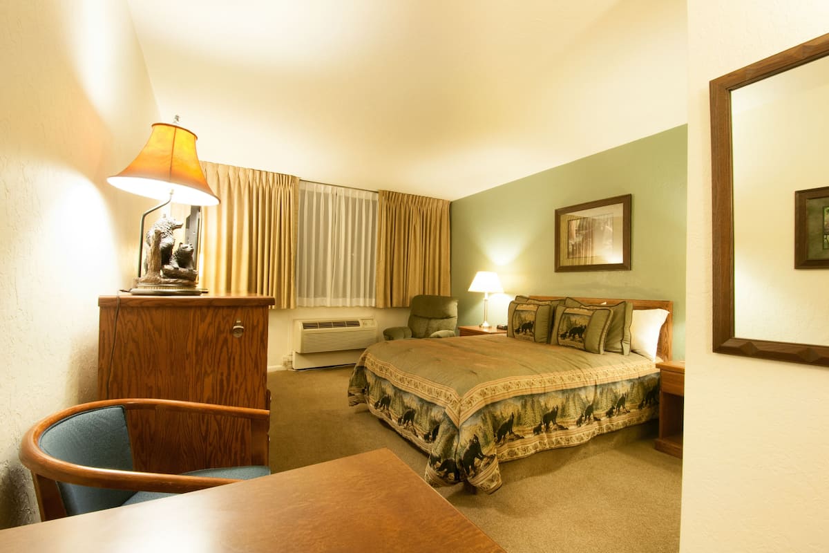 A hotel room with a bed, a desk, a chair, a lamp, and a picture on the wall.