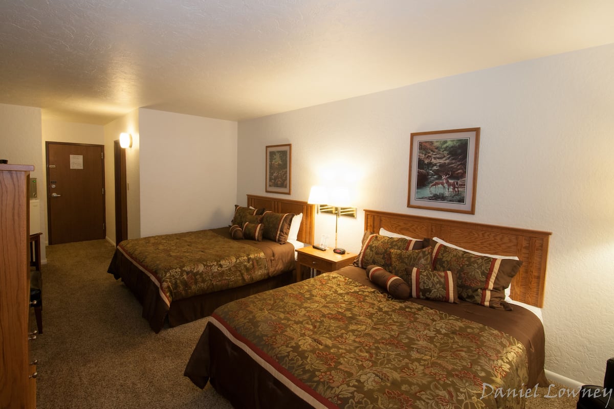A hotel room with two beds, a desk, a lamp, and a door.