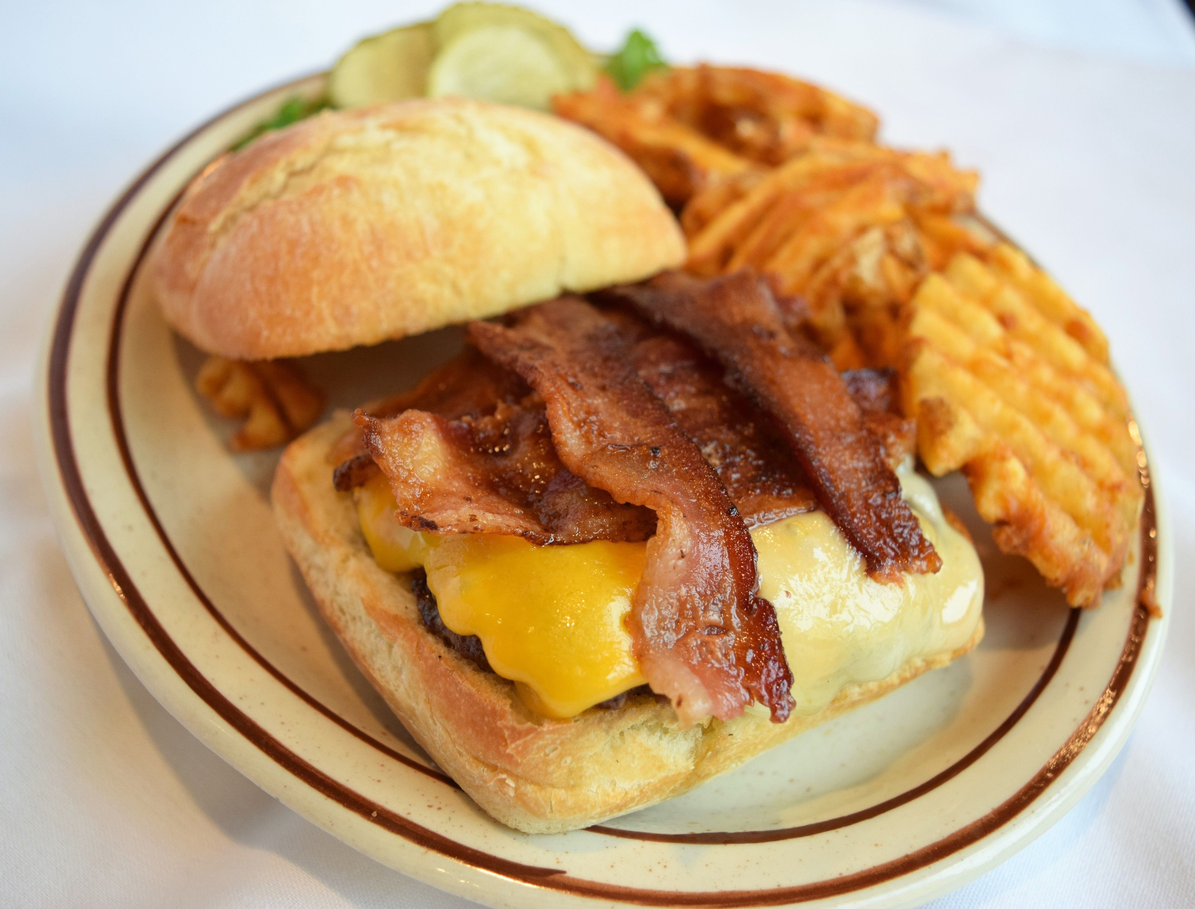 A sandwich with bacon and cheese on a bun, accompanied by fries and a pickle.