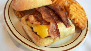 A sandwich with bacon and cheese on a bun, accompanied by fries and a pickle.
