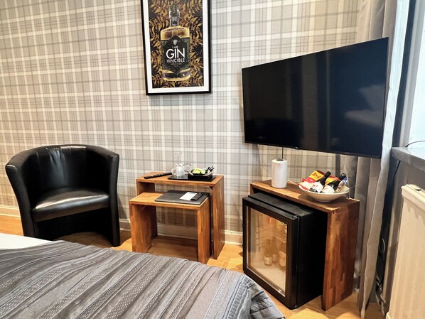A hotel room with a bed, a black leather chair, a small wooden table with a glass, a remote control, and a television on a stand. - Hotel Wictoria (Mariestad)