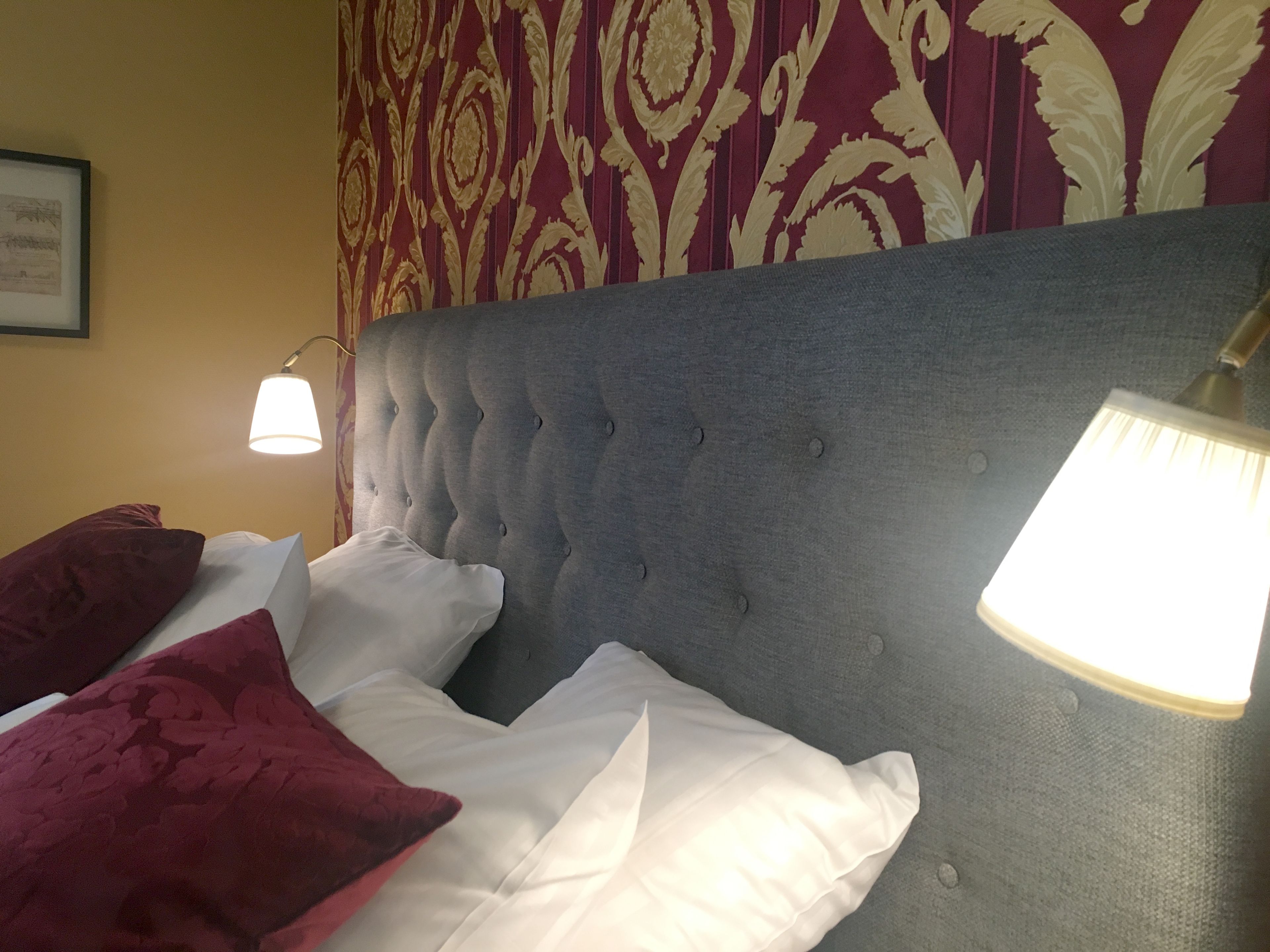A hotel room with a tufted headboard, white bedding, and a patterned wall.