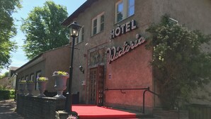 A hotel with a red carpeted entrance, a sign reading "HOTEL Victoria," and large flower pots on the steps. - Hotel Wictoria (Mariestad)