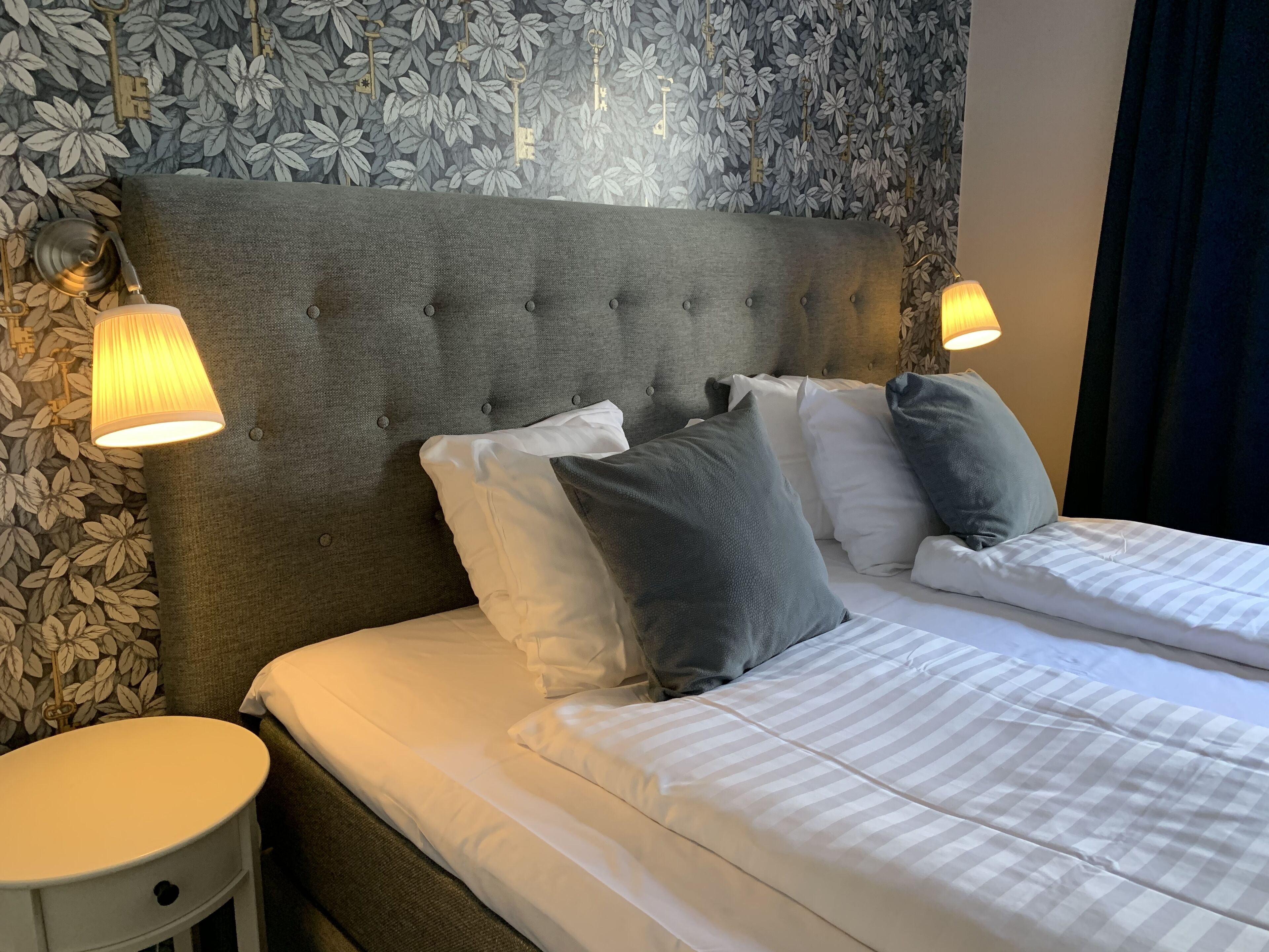 A double bed with white and gray striped bedding, a tufted headboard, and two bedside lamps.