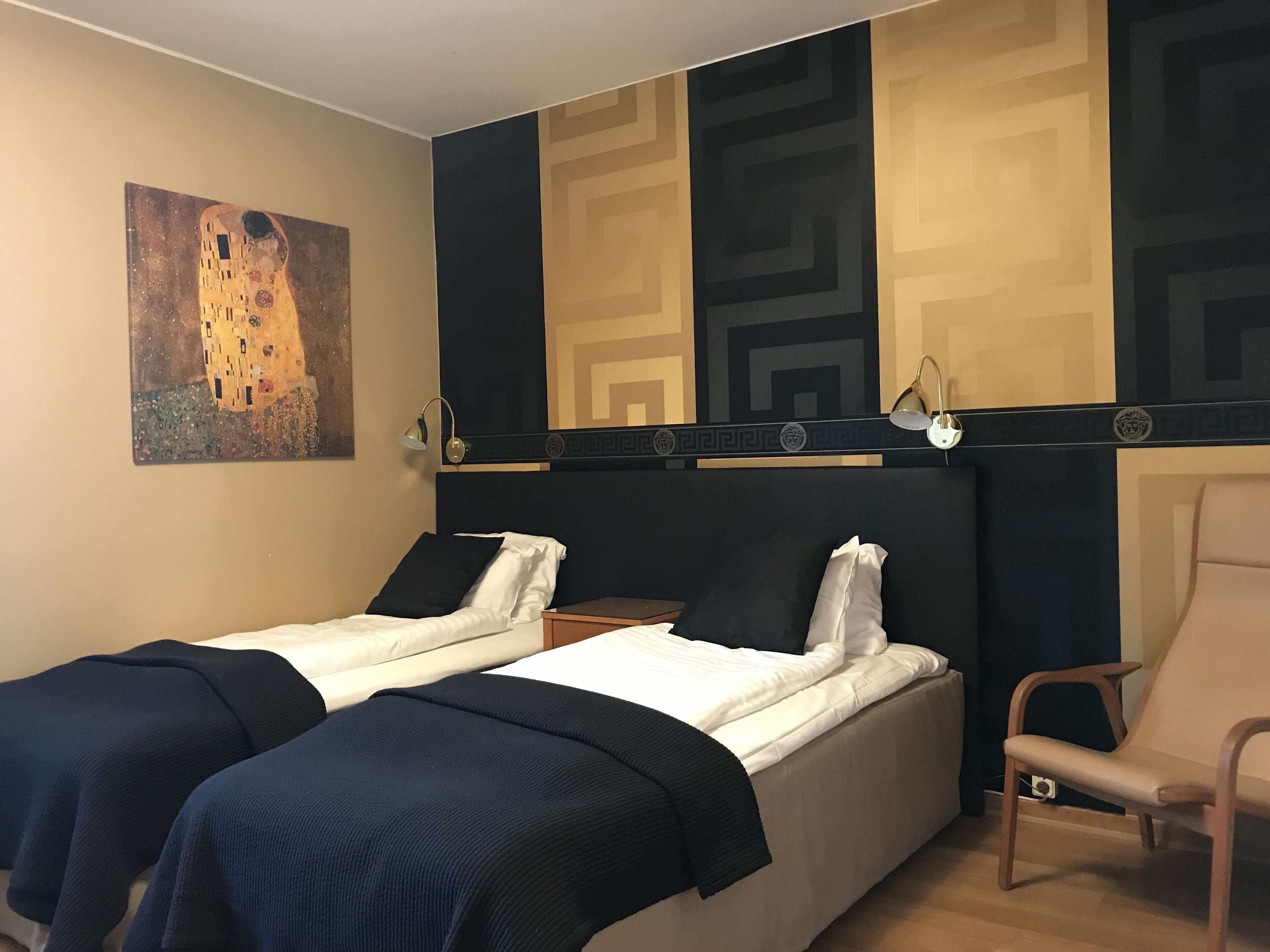 A hotel room with two beds, a chair, and a painting on the wall.
