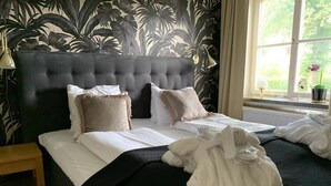 A neatly made bed with a dark headboard, white linens, and a black bedspread. There are two pillows, one white and one beige. A white bathrobe is draped over the bed. - Hotel Wictoria (Mariestad)