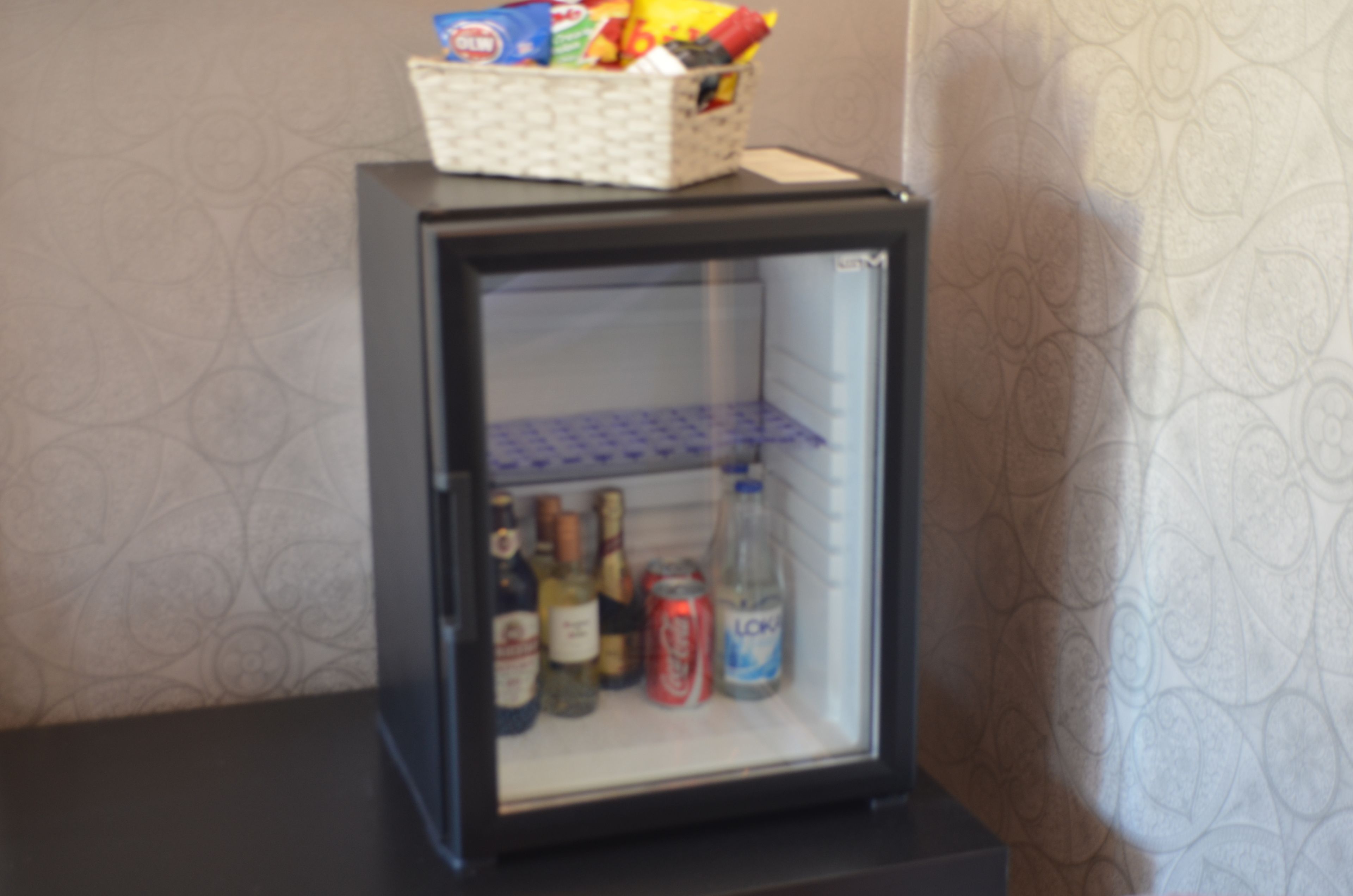 A small refrigerator with a basket on top containing snacks. Inside the fridge, there are various beverages and bottles.
