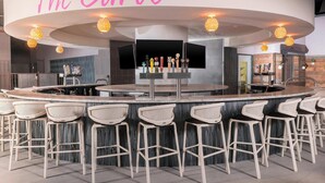 Eine Bar mit einer gebogenen Theke, mehreren Hockern und einem Schild mit der Aufschrift 'The Curve'.