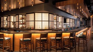Eine Bar mit einer langen Theke, mehreren Hockern und Regalen voller Flaschen.