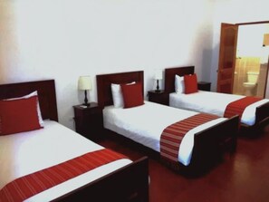 A hotel room with three single beds, each with a red pillow and a white bedspread. There is a wooden headboard on each bed, and a small bedside table with a lamp. - Casa La Merced (Granada)