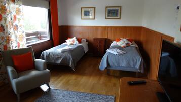 Una habitación de hotel con dos camas individuales, un cabecero de madera, un escritorio pequeño con un televisor, una silla y una ventana con cortinas.