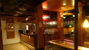 A bar area with a counter, stools, and a brick wall. There are hanging lights and a neon sign. - Botnia Hotel & Restaurant (Kronoby)