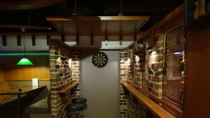 A narrow bar area with brick walls, a dartboard, and bar stools. - Botnia Hotel & Restaurant (Kronoby)