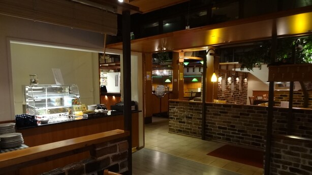A restaurant with a counter, tables, and chairs. There is a kitchen area in the background. - Botnia Hotel & Restaurant (Kronoby)