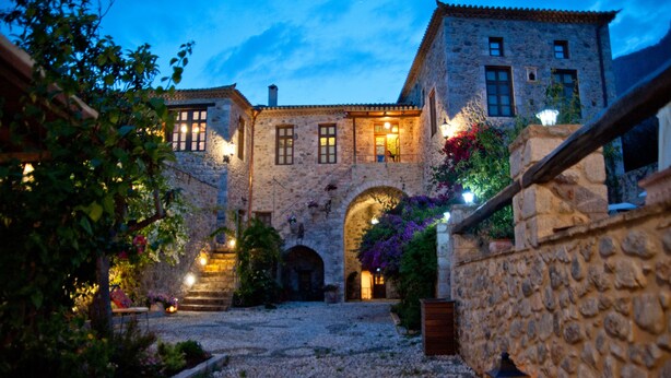 A stone building with a courtyard, arched entrance, and outdoor lighting. - Archontiko Hatzipanayiotis (South Kynouria)