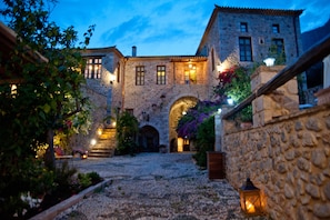 A stone building with a courtyard, arched entrance, and outdoor lighting. - Archontiko Hatzipanayiotis (South Kynouria)