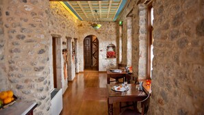 A stone-walled corridor with a wooden ceiling, a dining area with a table and chairs, and a window with a view. - Archontiko Hatzipanayiotis (South Kynouria)