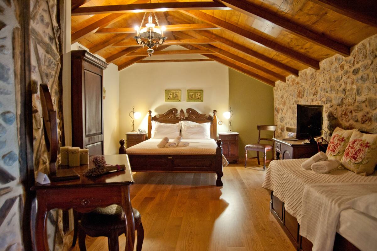 Een slaapkamer met een houten plafond, een groot bed, een bureau en een televisie.