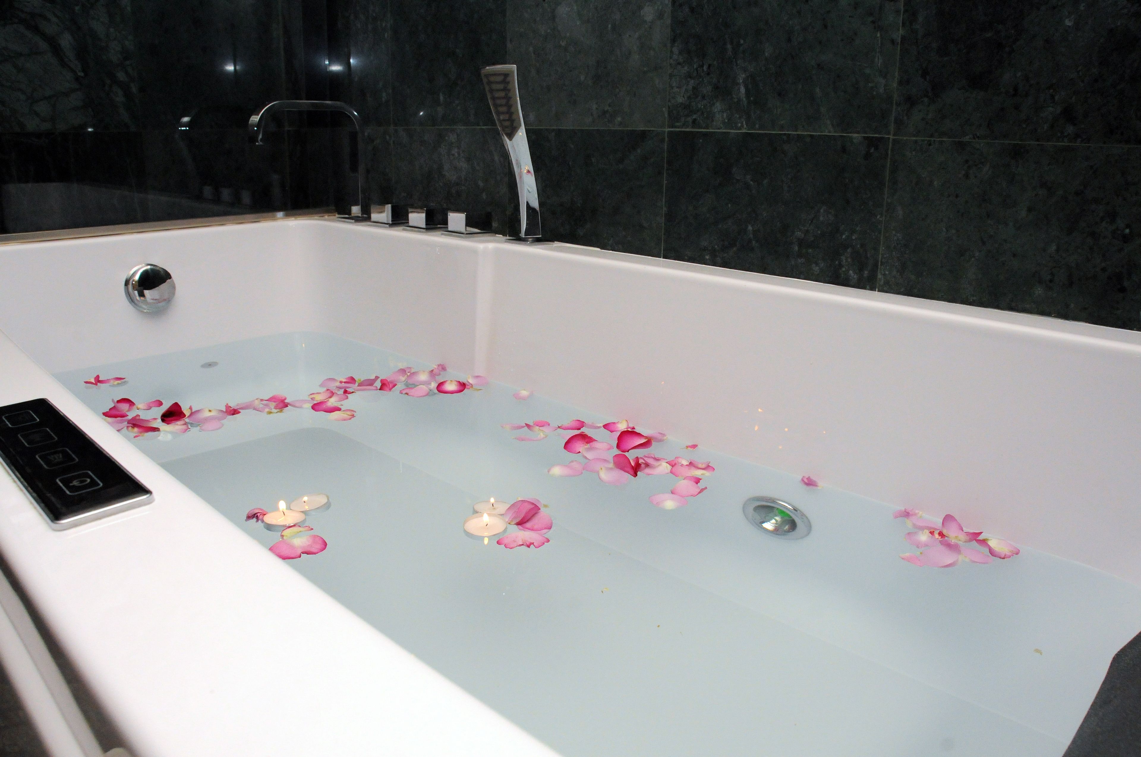 A bathtub with rose petals and candles, a control panel, and a shower head.