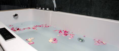 A bathtub with rose petals and candles, a control panel, and a shower head.