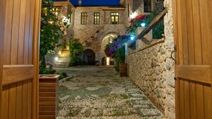 A stone building with a courtyard, wooden gates, and a stone wall with climbing plants. - Archontiko Hatzipanayiotis (South Kynouria)