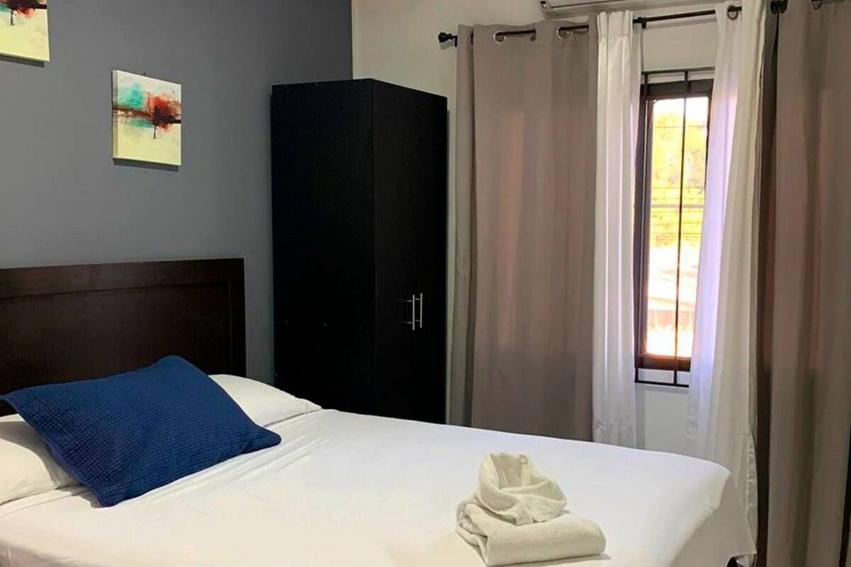 A hotel room with a bed, a wardrobe, and a window with curtains.