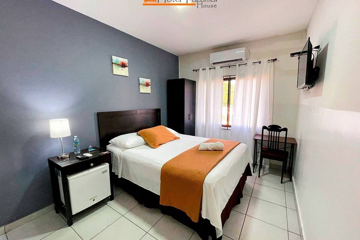 A hotel room with a bed, bedside table, lamp, and a chair.