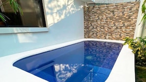 Ein moderner Außenpool mit klarem, blauen Wasserspiel, umgeben von einer weißen Mauer und einer Mauer im Steinoptik.