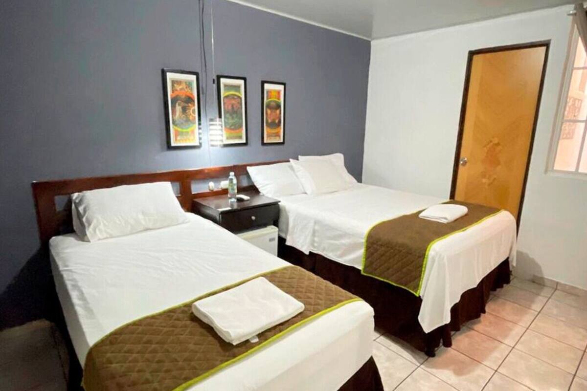 A hotel room with two beds, a nightstand, a wooden door, and three framed pictures on the wall.