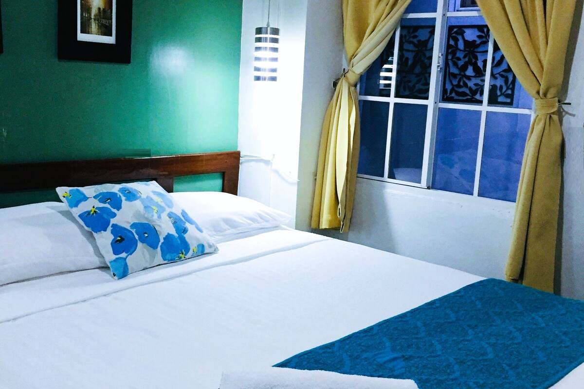 A hotel room with a bed, a picture on the wall, and a window with curtains.