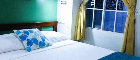 A hotel room with a bed, a picture on the wall, and a window with curtains.