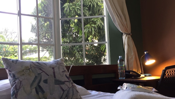 Ein Hotelzimmer mit einem Bett, einem Fenster mit Vorhängen, einem Nachttisch mit Lampe, einer Flasche und einem Telefon.