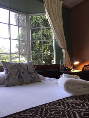 A hotel room with a bed, a window with curtains, a bedside table with a lamp, a bottle, and a phone. - Hotel Tazumal House (San Salvador)