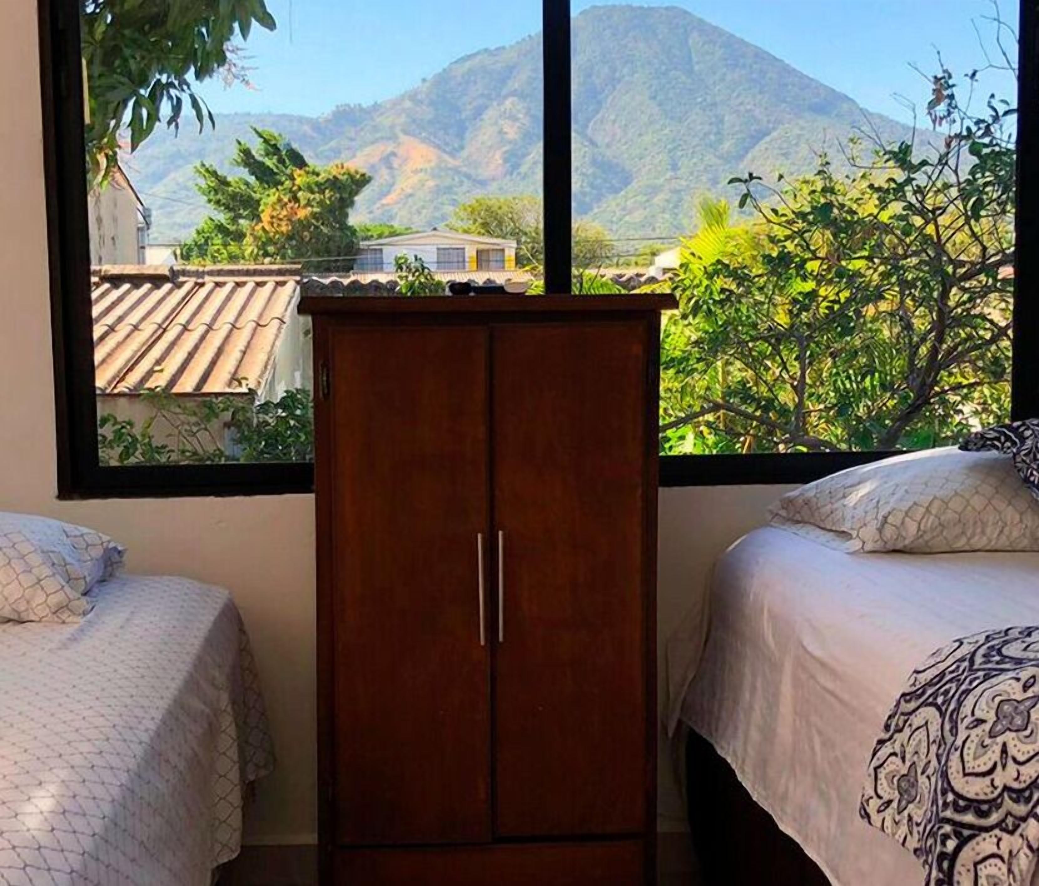 A bedroom with two beds, a wooden wardrobe, and a window with a mountain view.