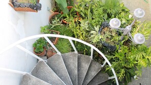 Eine Wendeltreppe mit weißer Handläufe, umgeben von verschiedenen Blumentöpfen und einem gefliesten Boden.