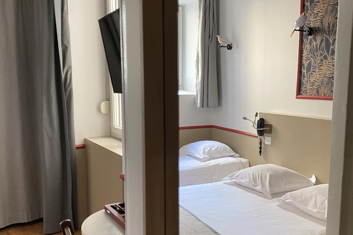 A bedroom with a bed, a window with curtains, a wall-mounted telephone, and a decorative panel.