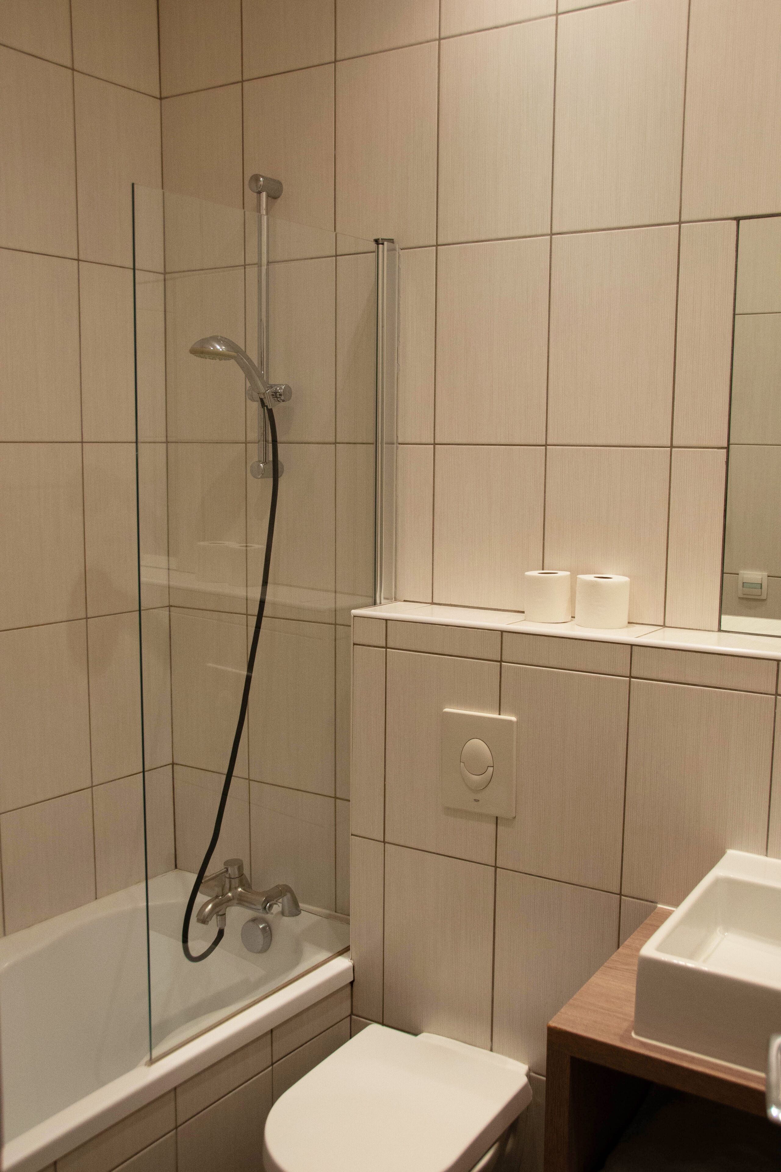 Een moderne badkamer met een glazen douchecabine, een wit toilet en een houten wastafelmeubel met een wastafel.