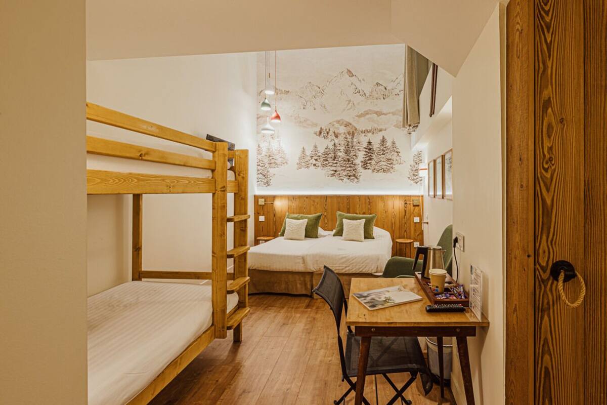 A dormitory room with bunk beds, a wooden desk, and a bed with green pillows.