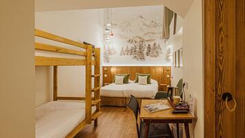 A dormitory room with bunk beds, a wooden desk, and a bed with green pillows.