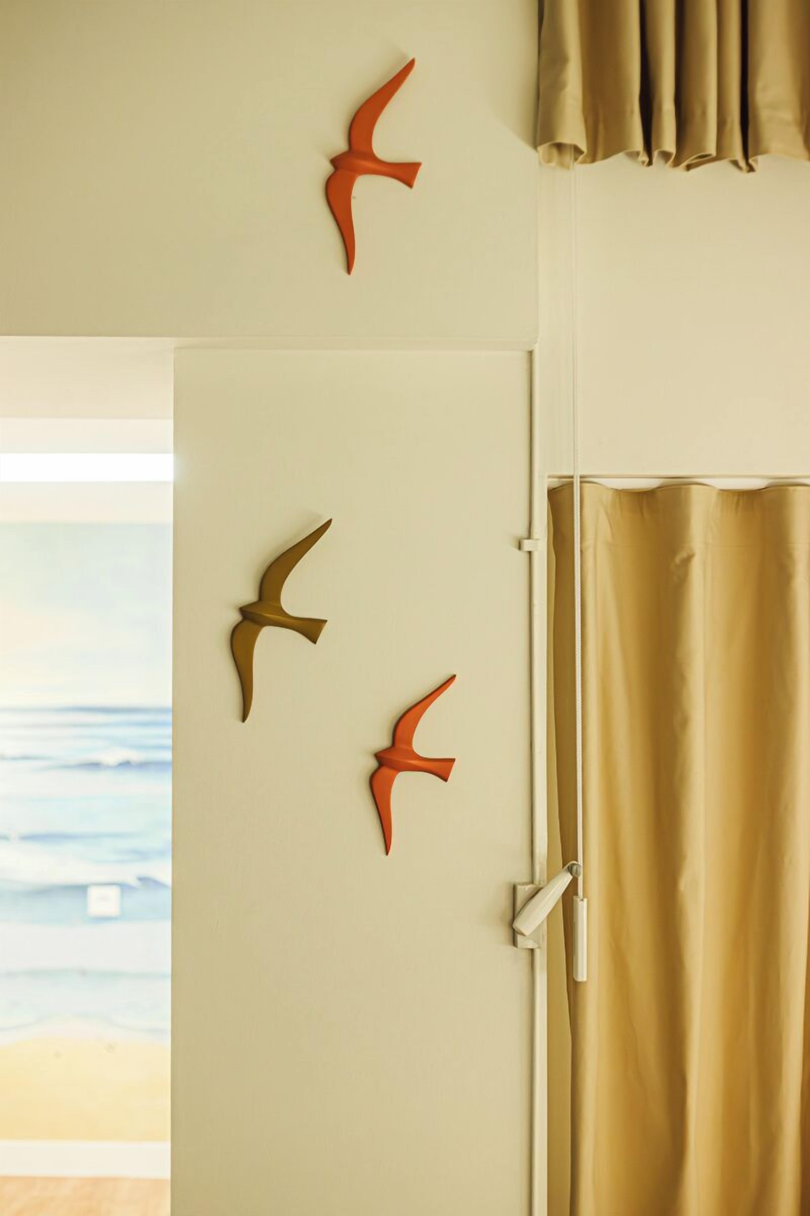 Ein Zimmer mit einer beigen Tür, einem beigen Vorhang und drei vogelähnlichen Wanddekorationen.