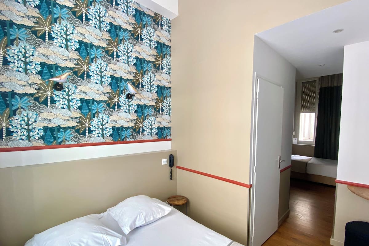 A bedroom with a bed, a wall-mounted telephone, and a door leading to another room.
