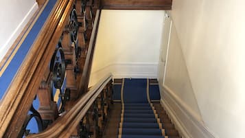 Una escalera de madera con escalones alfombrados en azul y barandillas de metal decorativas.
